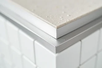 Gros plan sur une cornière en aluminium brossé installée entre un carrelage blanc et un plan de travail gris dans une cuisine moderne