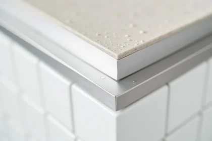 Gros plan sur une cornière en aluminium brossé installée entre un carrelage blanc et un plan de travail gris dans une cuisine moderne