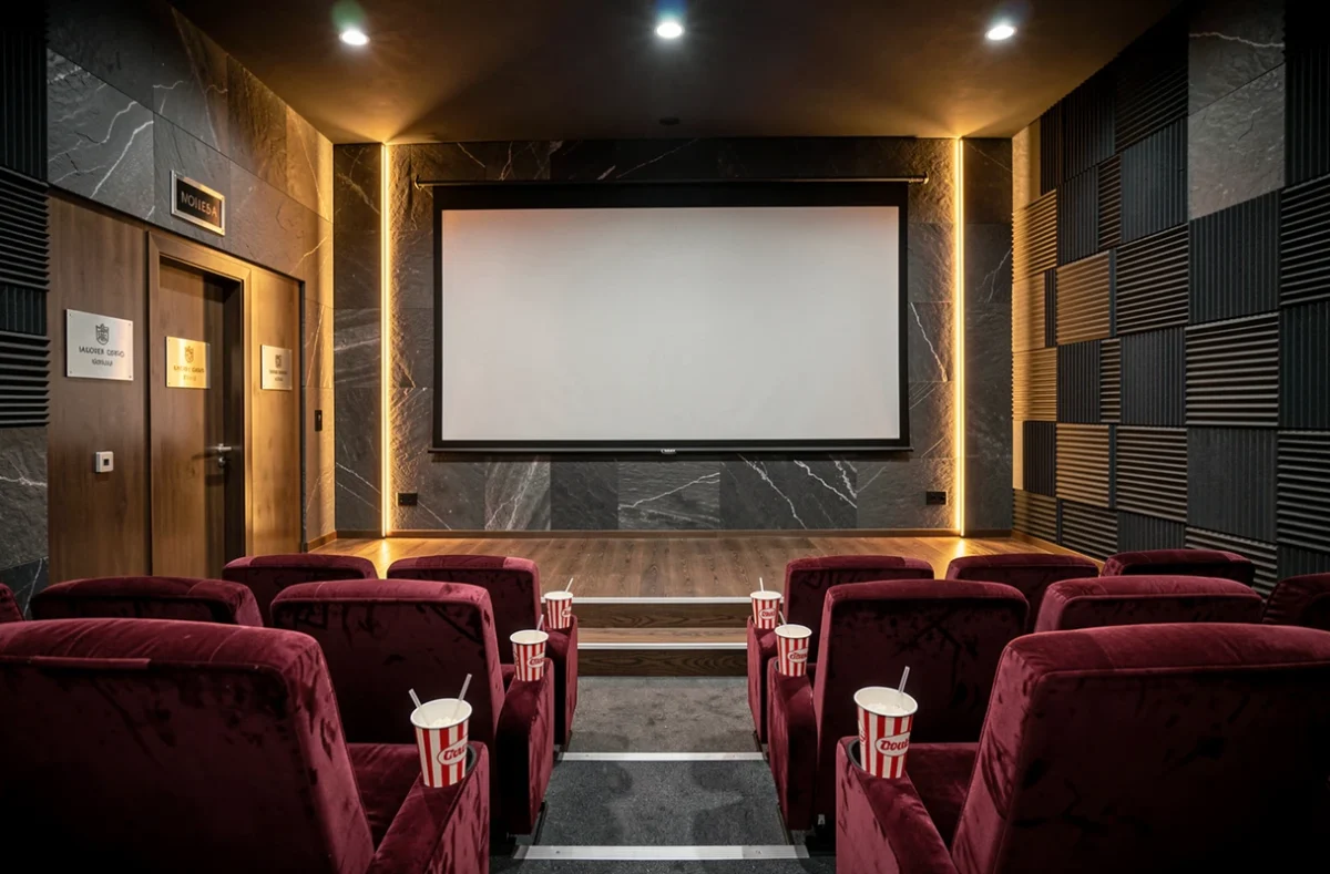 Salle de cinéma privée à domicile avec fauteuils en velours bordeaux, écran de projection et décoration murale thématique